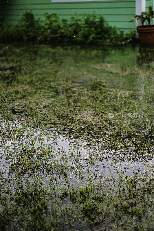 暴雨袭击了一个独栋房屋的屋顶，屋顶上有排水沟，热带风暴淹没了院子