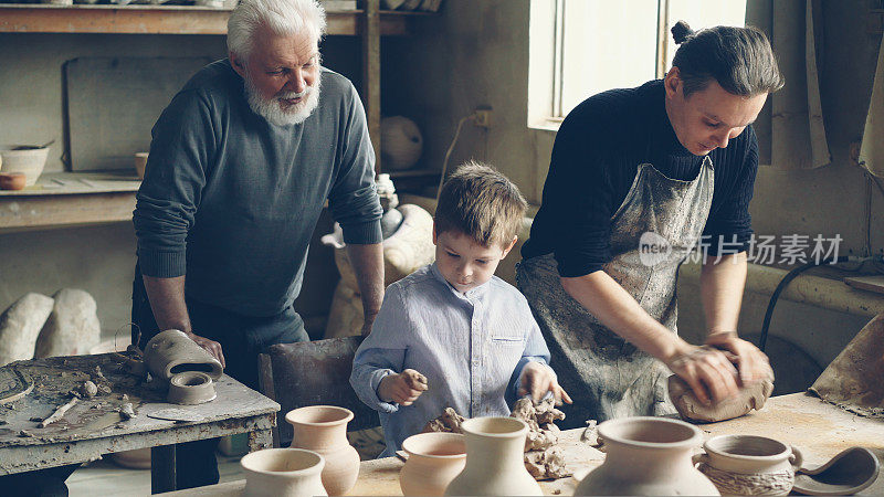 职业陶工在家庭工作室的工作台上揉泥，儿子在帮他，年迈的父亲在后面看着他们。小型家族企业的概念。