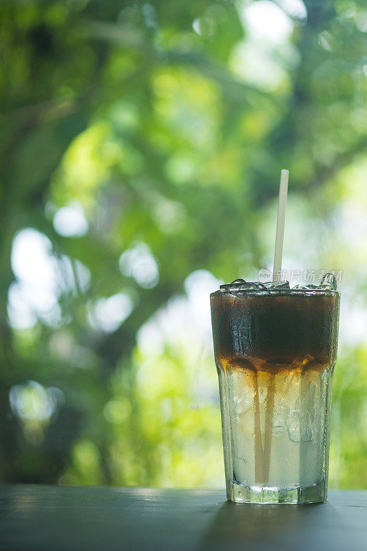 玻璃杯中的冰美式咖啡，在自然背景下呈现出两层黑咖啡和水