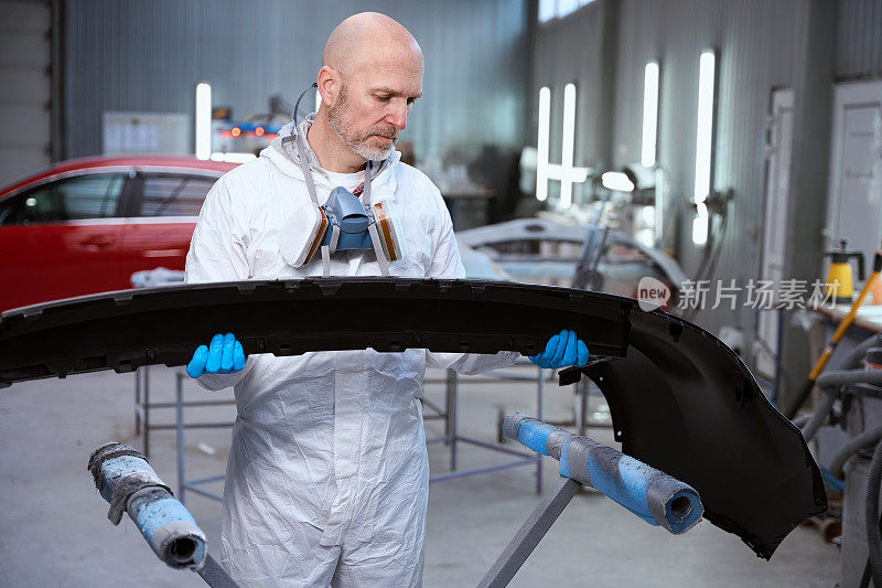 一名戴着防护手套的中年男子正在为涂装汽车车身部位做准备