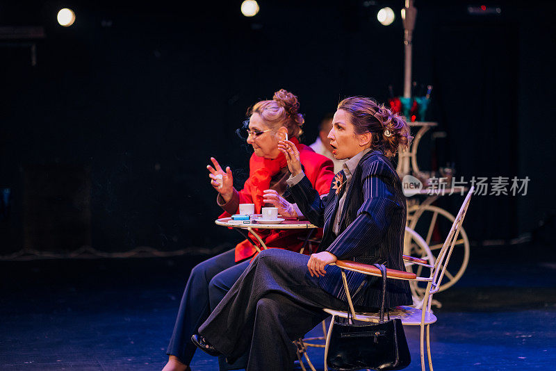 两个女演员在一个剧院的舞台上表演，场景被设置成一个咖啡店