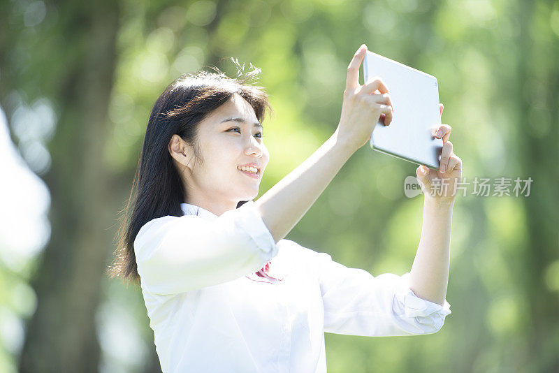 一名女学生手持平板电脑站在杨树旁