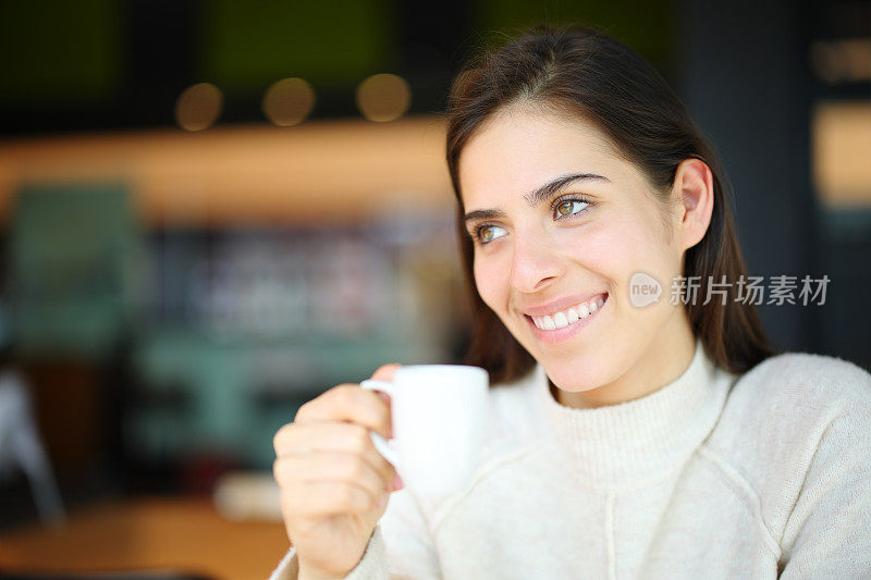 在咖啡店里，快乐的女人拿着杯子望向别处