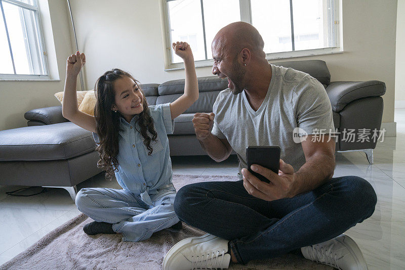 父亲和女儿在家里客厅的地毯上一起玩智能手机