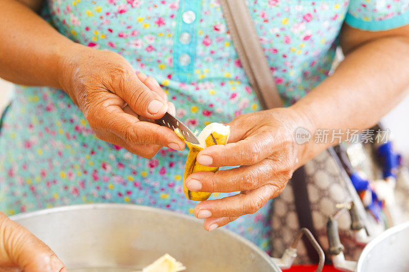 成熟的泰国妇女正在用刀剥小香蕉