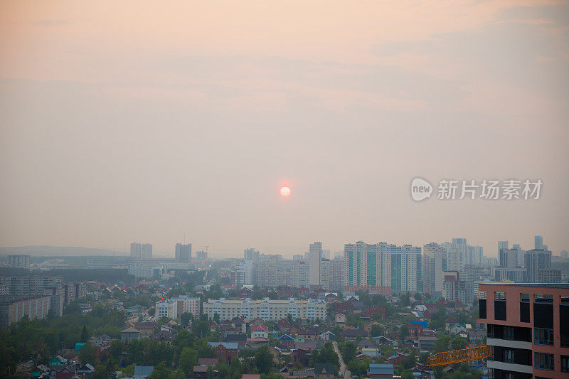 太阳在浓重的烟雾中笼罩着城市、房屋、建筑物、摩天大楼。城市全景，森林大火的烟雾，环境问题，灾难