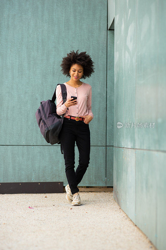 一名非洲裔美国妇女拿着手机和包走在绿墙边