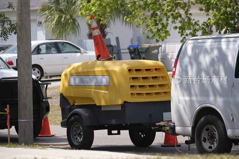 在道路施工现场，有黄色压缩机拖车和手提钻的多功能货车