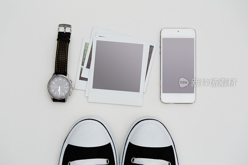 潮人文化项目。运动鞋、手机、空白的宝丽来式照片和一块手表平躺在白色的背景上
