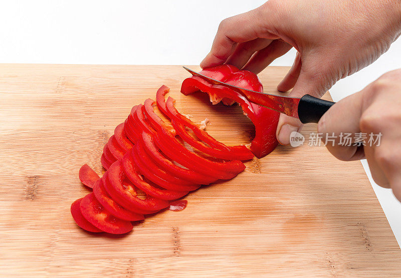 在厨房木板上用锋利的刀刃切甜椒。女性的手。从上面看。