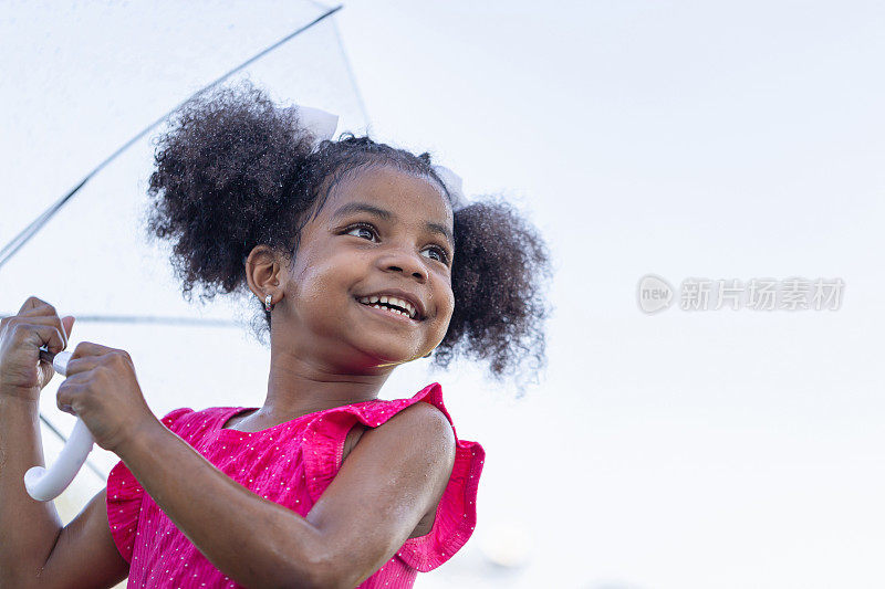 开朗的小女孩撑着伞在公园里打雨，可爱的小女孩在户外的花园里玩耍