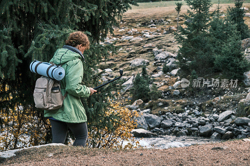 一位45岁的开朗的妇女正在山林中徒步旅行，并对着运动相机拍摄视频