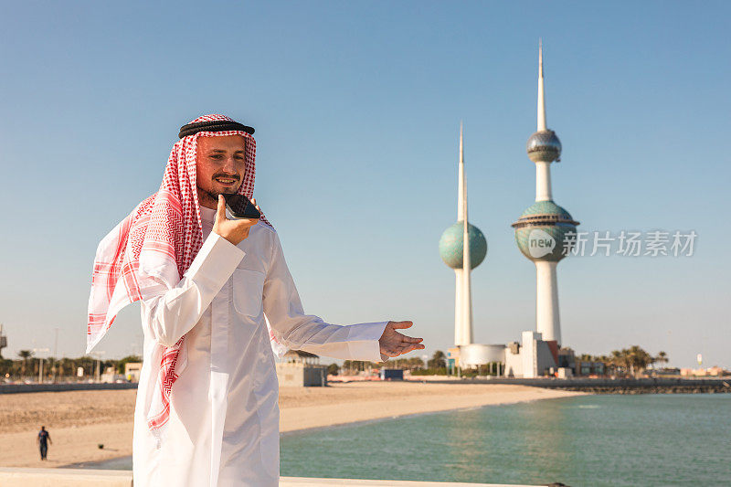 年轻的酋长正在打电话，背景是科威特的塔楼