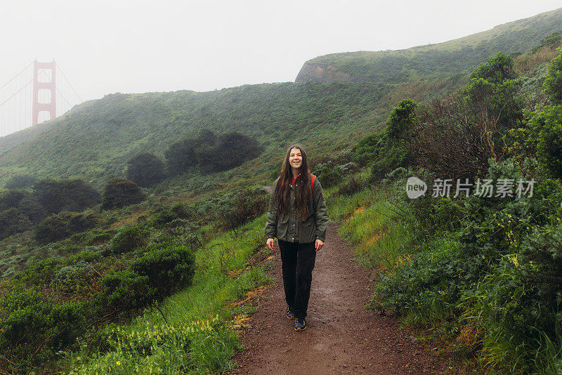 一个快乐的女人走在山上，可以看到旧金山的金门大桥