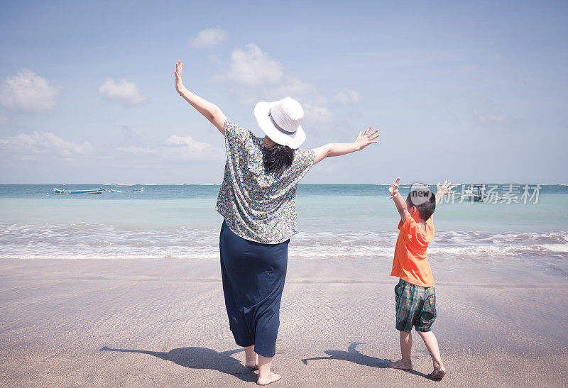 母亲和儿子在海滩上张开双臂