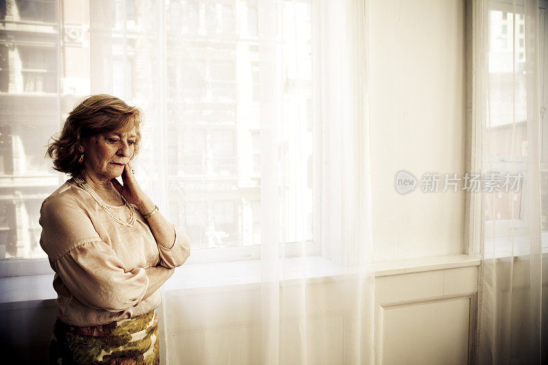 一位忧心忡忡的老妇人站在拉着窗帘的窗边