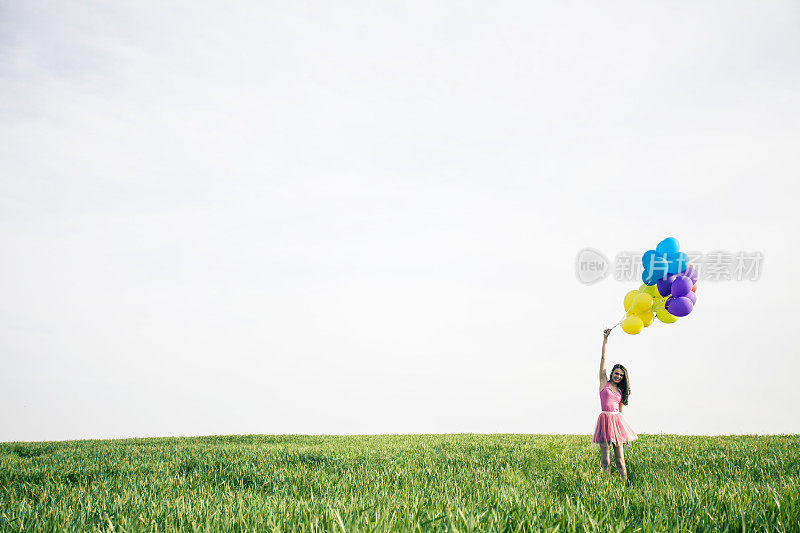 漂亮的年轻女子拿着气球走过草地