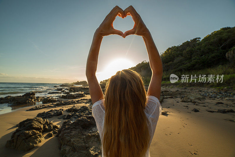 年轻女子把海滩上的夕阳画成心形