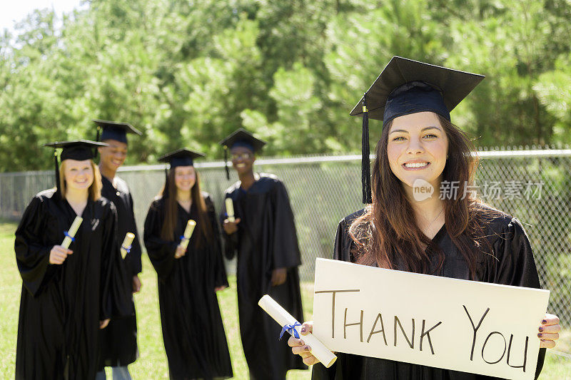 教育:一个拉丁女孩在毕业后举着“谢谢”的牌子。朋友。