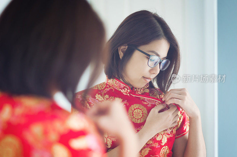 亚洲眼镜女人用镜子看她的旗袍。