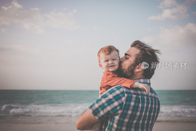 海滩日落时，爸爸抱着小男孩