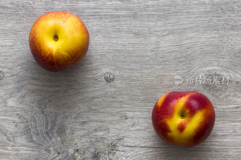 木桌上放着两个油桃。正上方的观点。