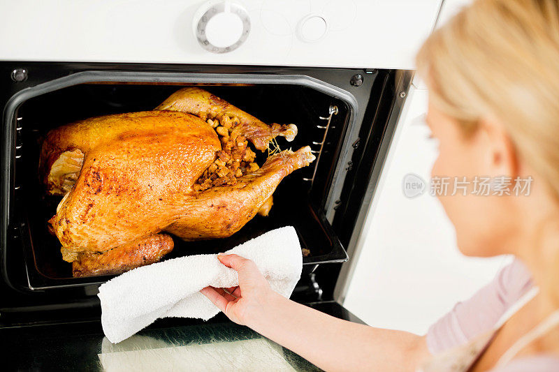 一个女人把火鸡从烤箱里拿出来。