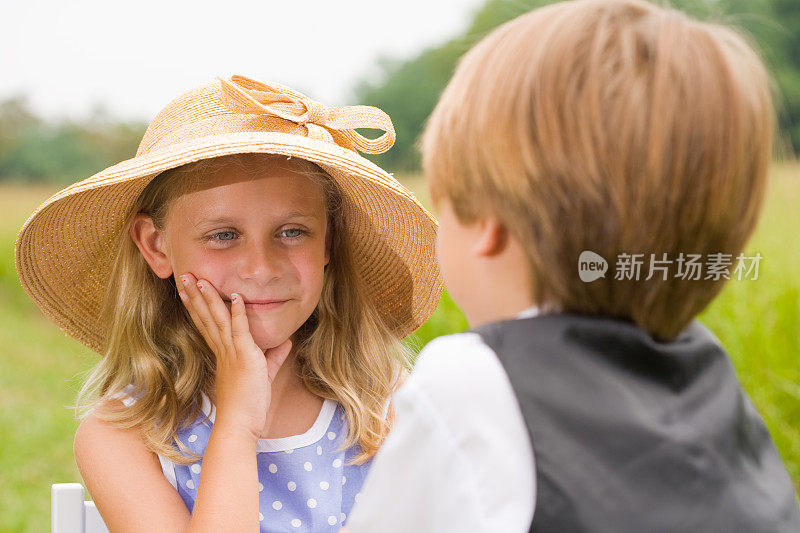 戴草帽的小女孩看着穿马甲的小男孩