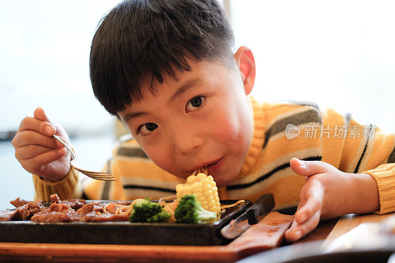 亚洲男孩在餐厅吃牛排