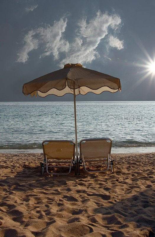 沙滩上有两把躺椅和一把阳伞