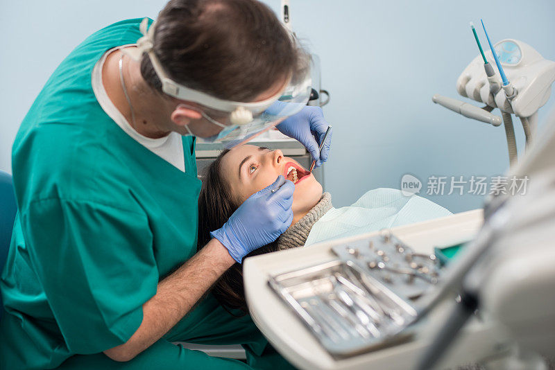男性牙医在牙科诊所使用牙科工具-镜子和探针检查病人的牙齿。医学、牙科和保健概念。牙科设备