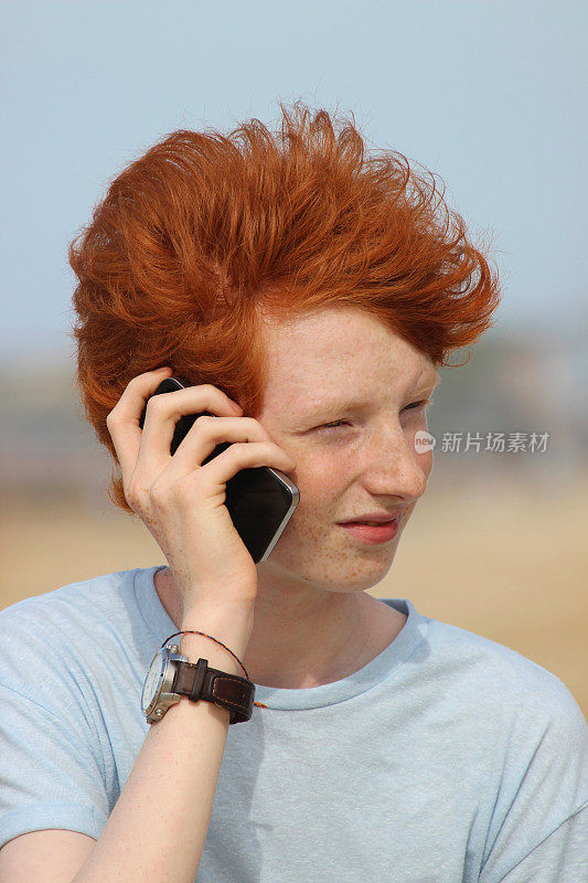 一个十几岁的男孩在用手机，说话，笑，海滩