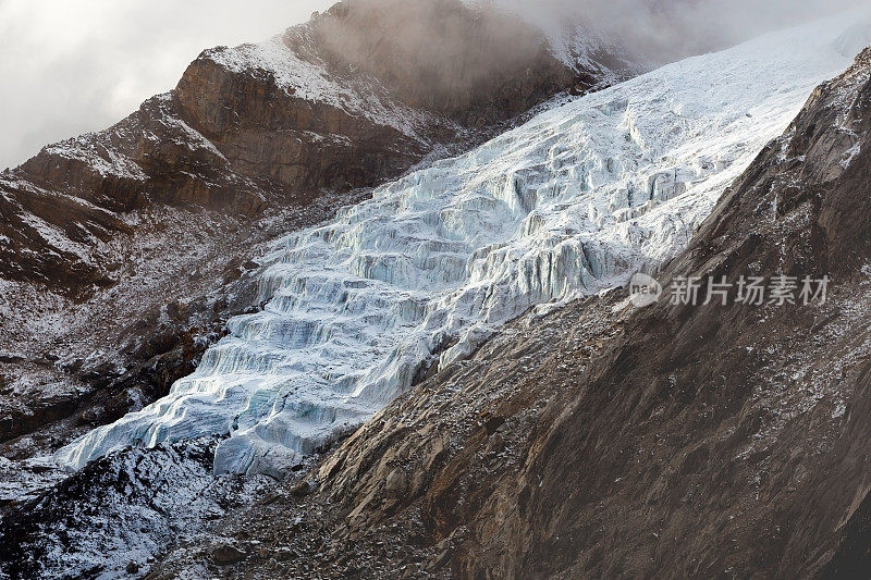 尼泊尔喜马拉雅山的冰川河。美丽的风景，一个白色的雪山冰川之间的两个岩石斜坡在雾和云。高山冰川的背景。