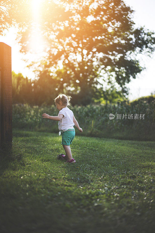 蹒跚学步的女孩在乡村农舍的草地后院里玩耍