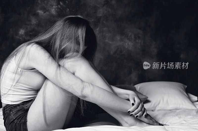 少女沮丧地坐在床上哭泣，把脸藏在膝盖里。黑白照片