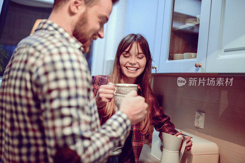 年轻夫妇在家里的厨房里微笑着煮咖啡