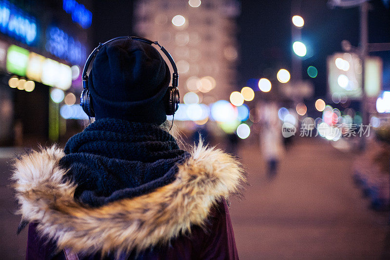 女孩走在夜晚的城市街道听着音乐