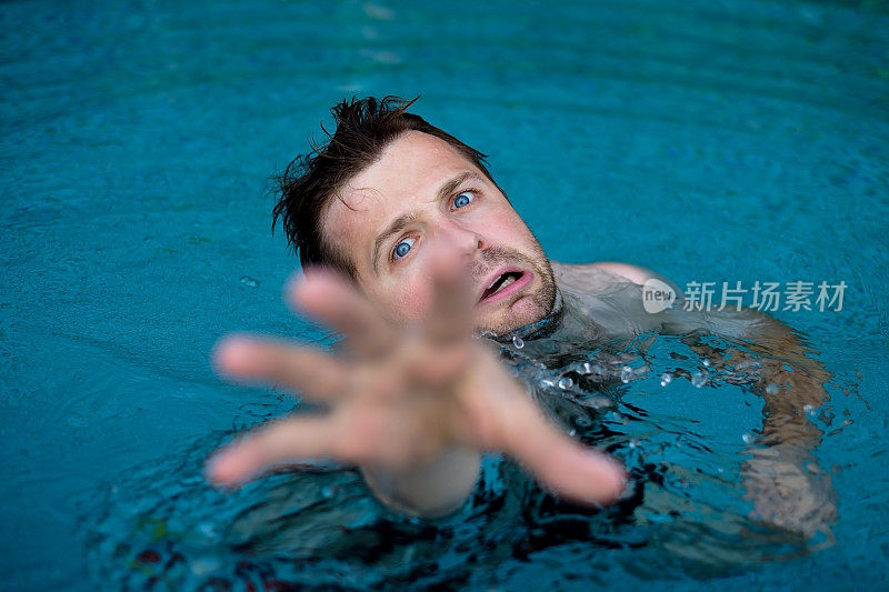 一个在游泳池里溺水的白人寻求帮助。他害怕地伸出双手。
