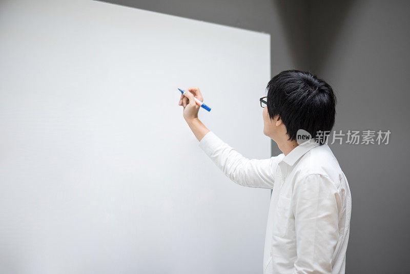 一个年轻的亚洲人在会议室的白板上写字