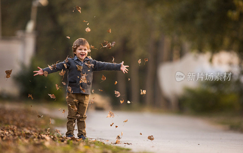 快乐的孩子玩的时候，扔秋天的树叶在公园里。