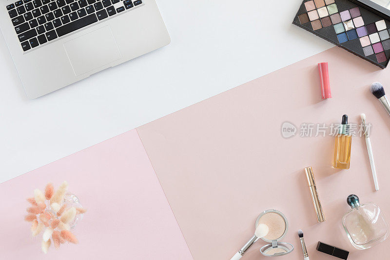 平躺和从上面看办公室桌子书桌框架。女性的工作空间与手机，笔记本电脑，化妆品，花在白色和粉色的柔和背景。