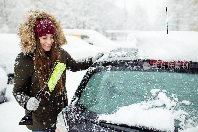 年轻女子在清理车上的积雪