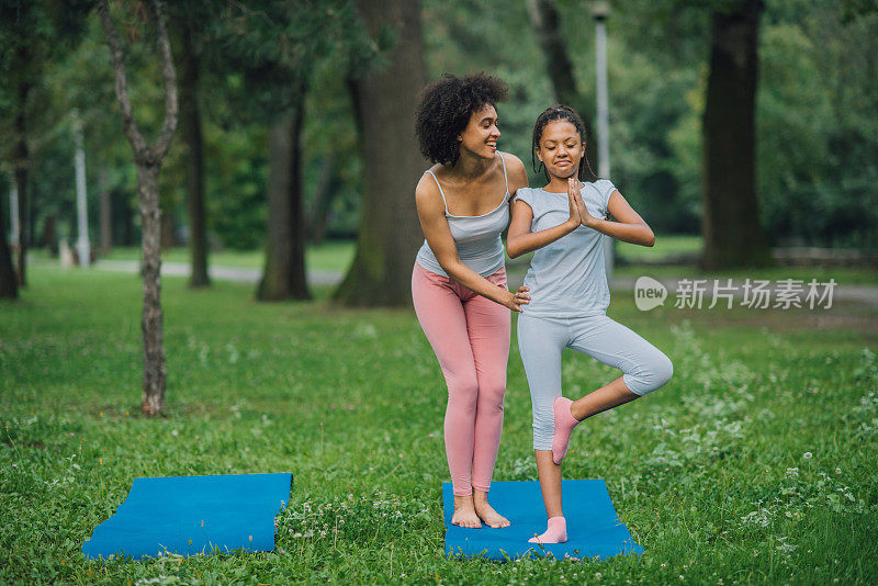 愉快的瑜伽教练协助年轻女孩在户外锻炼