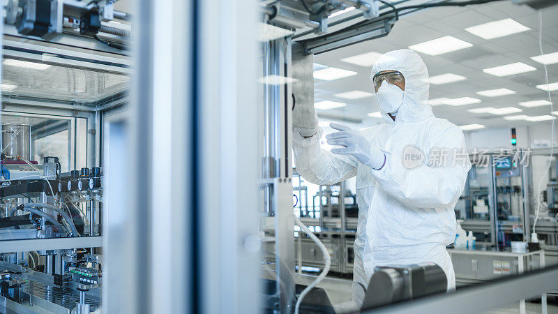 在制造设施拍摄的科学家在无菌防护服在现代工业3D打印机器上工作。制药、生物技术和半导体制造工艺。从里面。