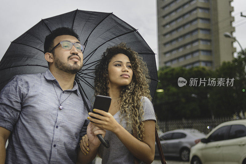 一对年轻夫妇在雨天等待通过手机应用程序预订的出租车