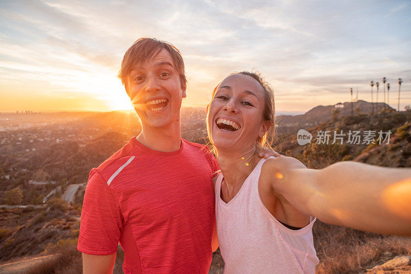 一对运动的年轻夫妇在日落时分在城市上方自拍