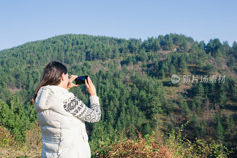 欣赏山景的年轻女人。年轻女子在山顶用手机拍摄风景