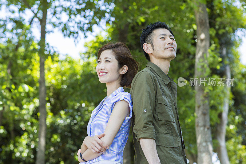 一对年轻夫妇背靠背站在公园里
