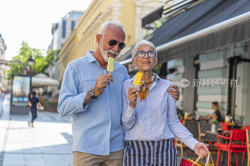 一对活跃的老年夫妇正在城市街道上散步，享受着冰淇淋