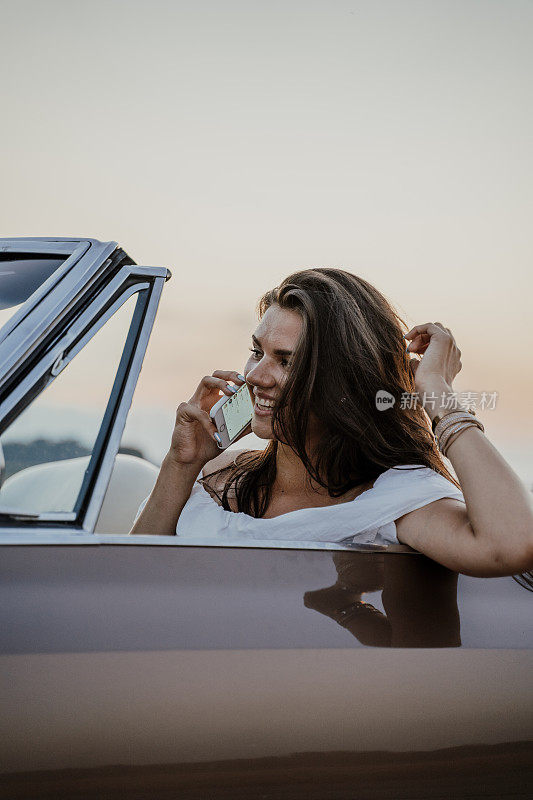 日落时分女人在敞篷车里打电话的肖像